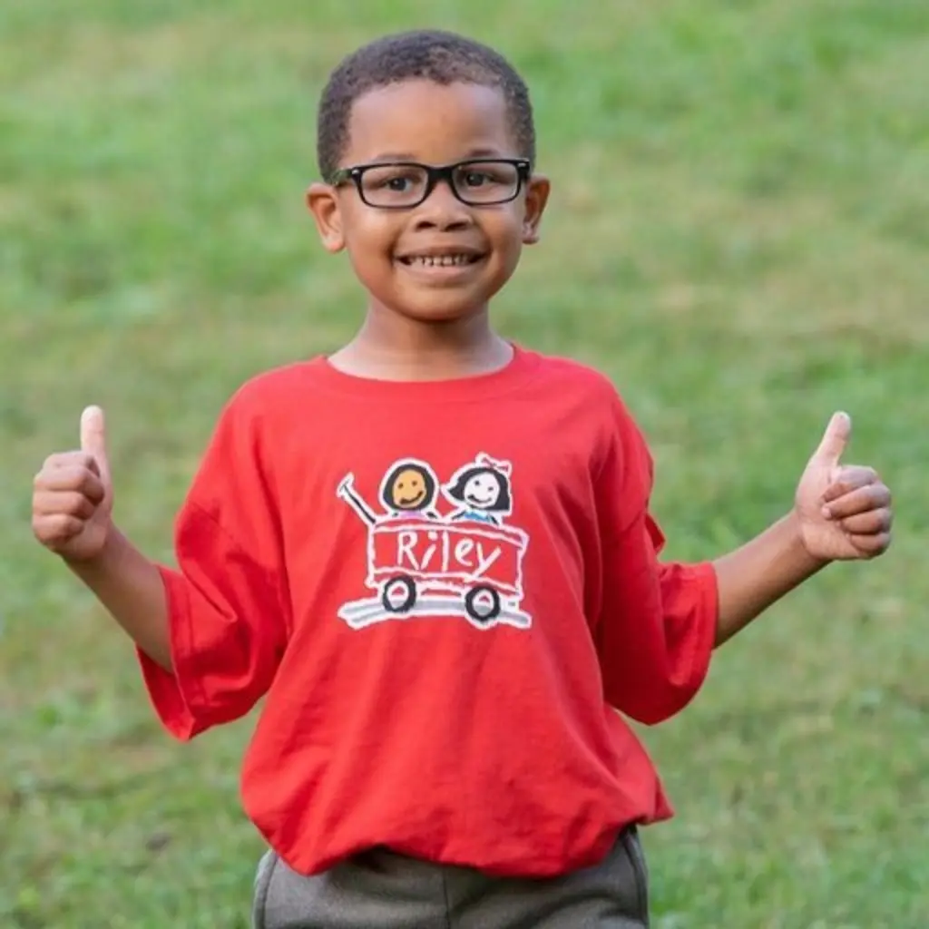 A child in a Riley t-shirt and giving two thumbs up
