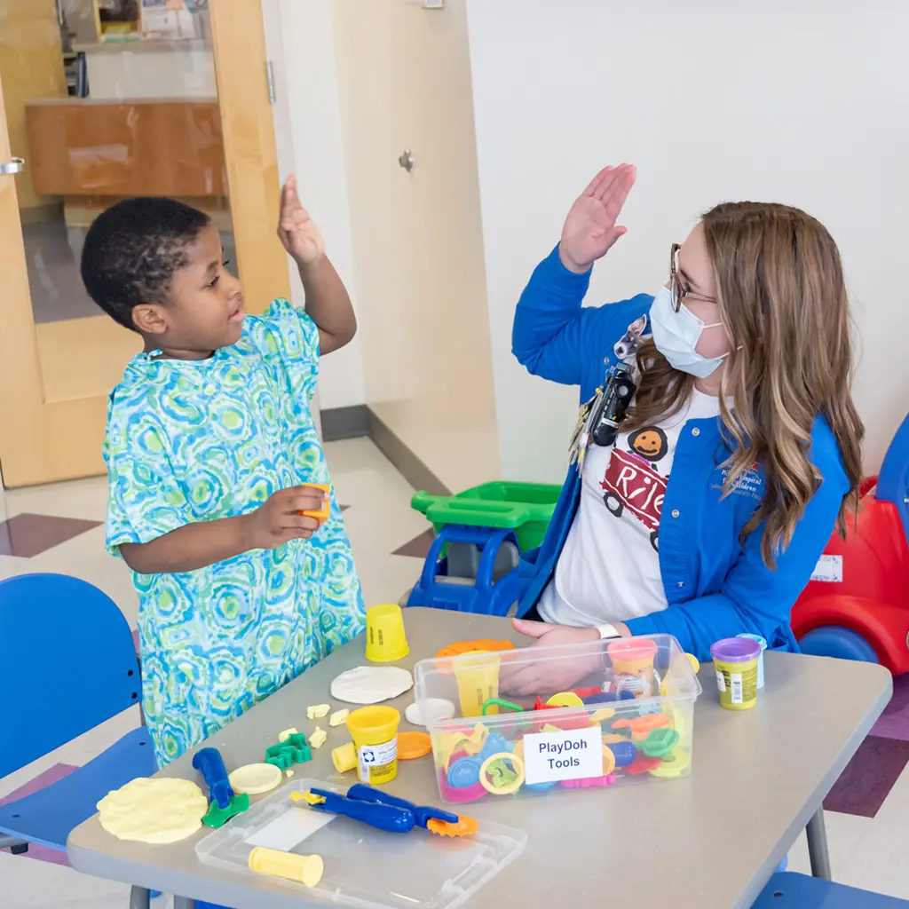 Riley Child Life Specialist giving a high five to a Riley boy patient in a Riley play room.