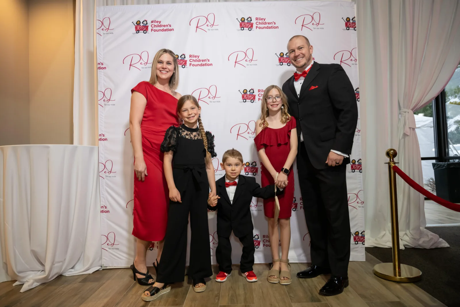 Riley family in front of backdrop with Riley logos at Red event