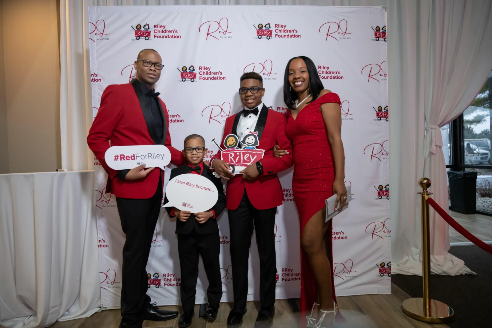 Riley family in front of backdrop with Riley logos at Riley Red event