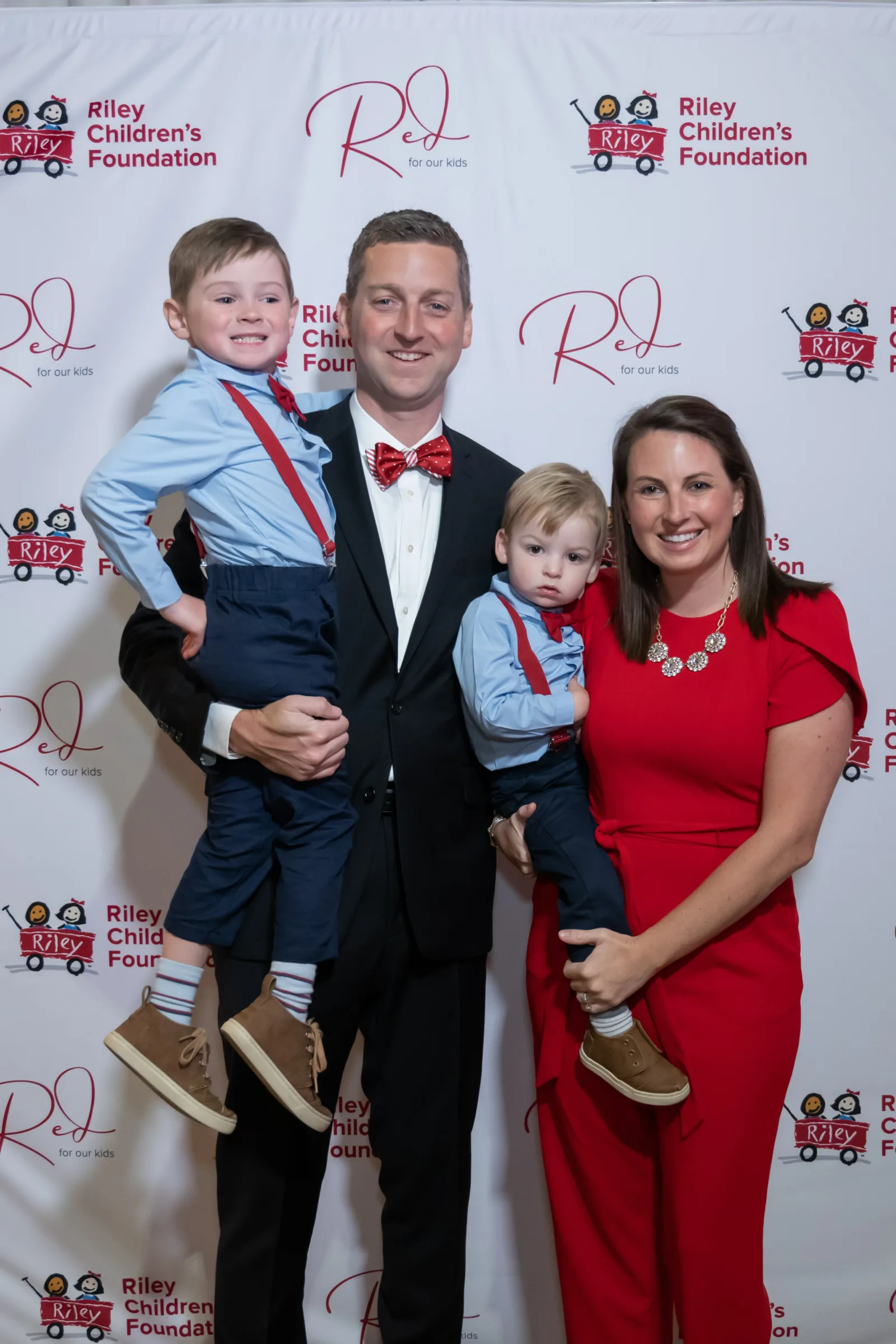 Riley family in front of backdrop with Riley logos at Riley Red event