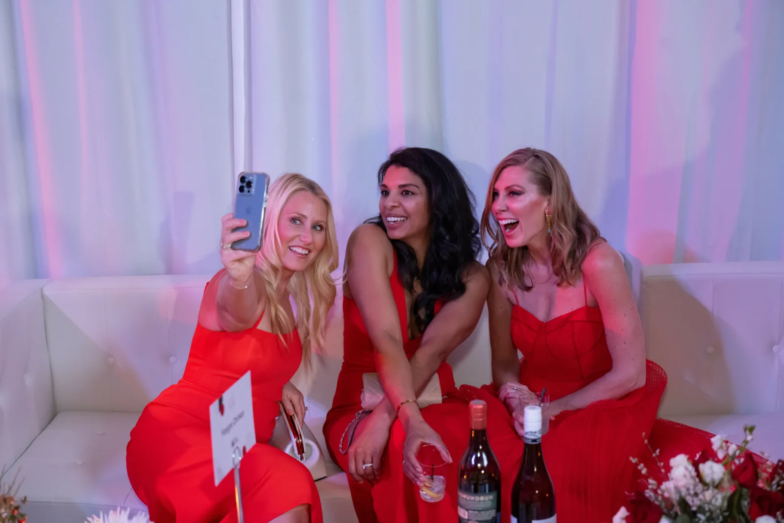 Women on couch wearing red dresses taking a selfie.