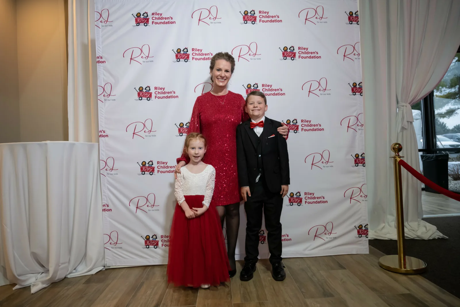 Riley family in front of backdrop with Riley logos at Riley Red event