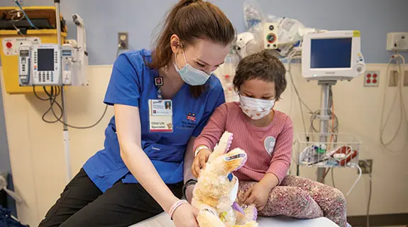 Child Life Specialist with sharing a plush rabbit toy with a Riley patient in hospital room.