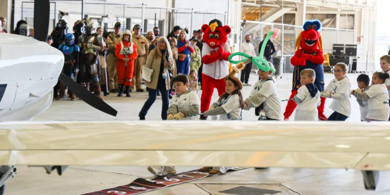 Image of kids and mascots pulling a plane.
